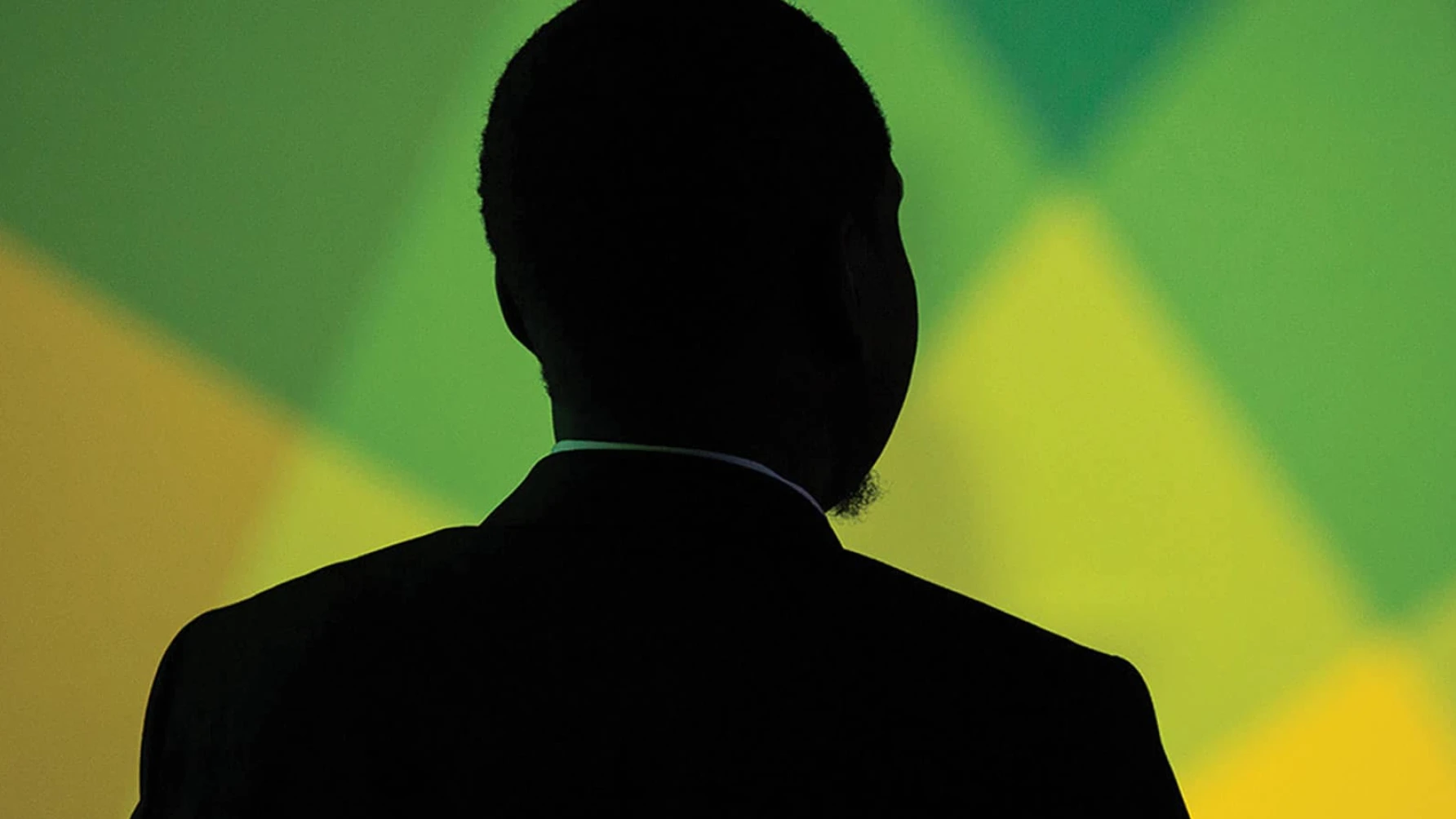 Silhouette of a man in a suit viewed from behind, standing against a vibrant, abstract green and yellow geometric background. The lighting casts the subject entirely in shadow, creating a dramatic and contemplative atmosphere.