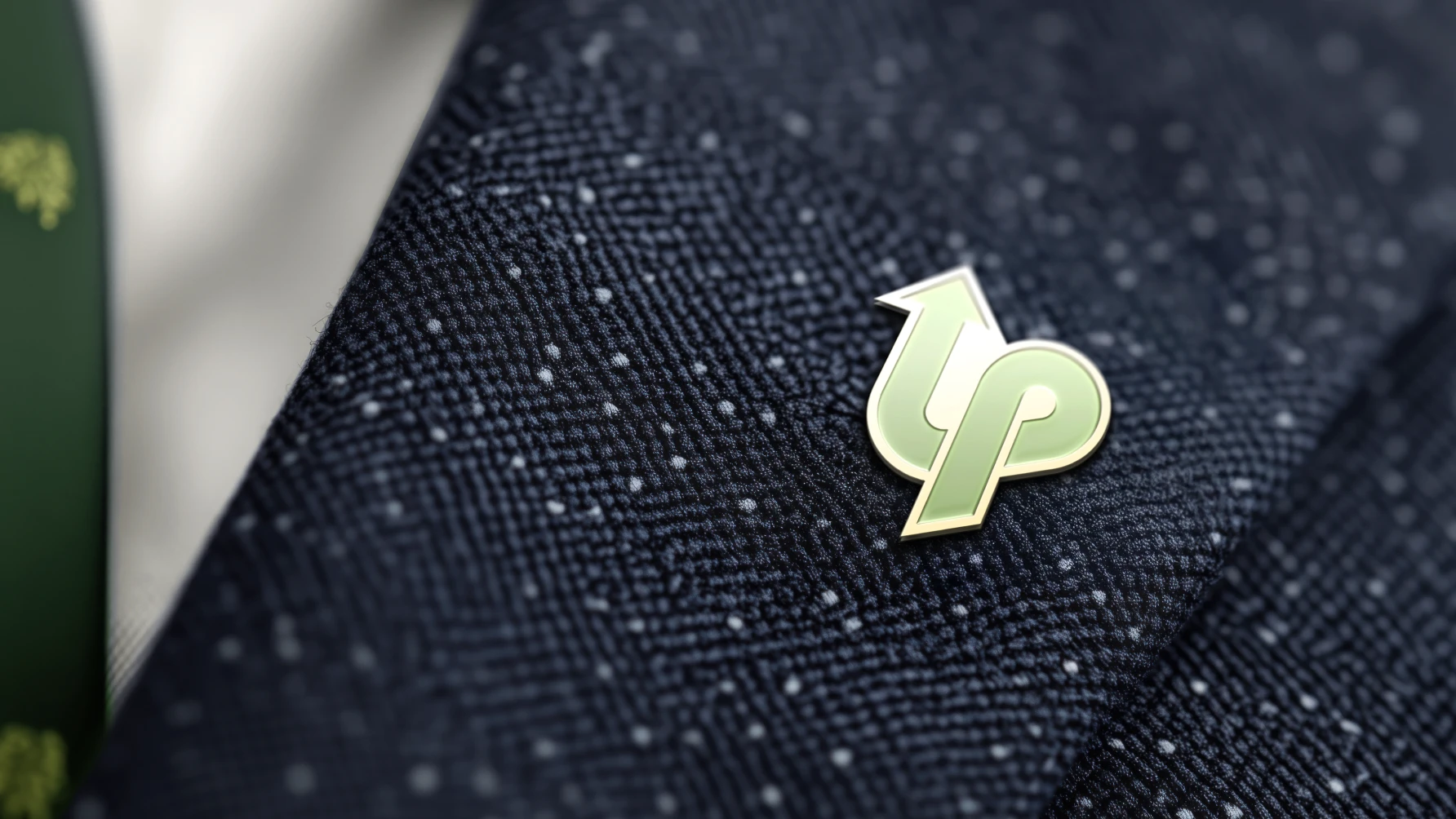 The image shows a close-up of a lapel pin on a dark navy textured suit jacket. The Latino Prosperity pin features a stylized, glossy logo that appears to be two interlocking arrows forming the letters "l" and "p" in a modern design. The arrows are light green with a subtle gradient and outlined in a soft metallic gold, conveying a sense of growth or forward movement.